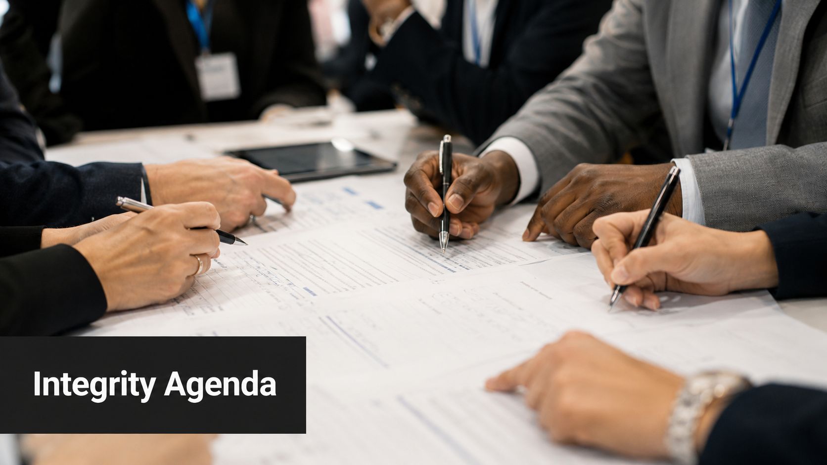 A diverse group of professionals working together around a table on a business integrity agenda document.